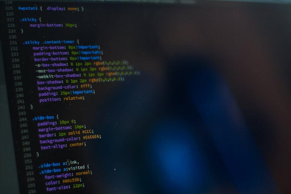 Photograph of a computer screen displaying lines of programming code with colorful syntax highlighting, including various keywords, variables, and functions in a dark-themed coding interface. The scre